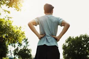 dolor de espalda de los corredores después de trotar en el parque con puesta de sol foto