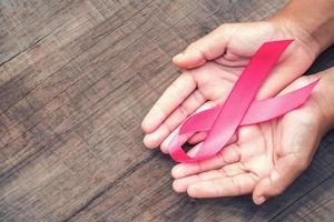 concepto de salud y medicina. mano que sostiene la cinta rosa en la madera. conciencia del cáncer de mama. señal de esperanza foto