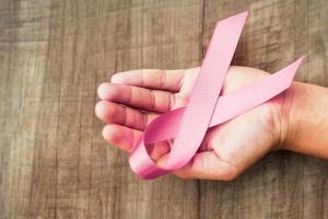 concept healthcare and medicine. hand holding pink ribbon on wood. breast cancer awareness. sign of hope photo