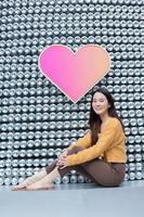 una bella mujer asiática con el pelo largo está sentada y sonriendo en el fondo del corazón como concepto del día de san valentín. fondo abstracto foto