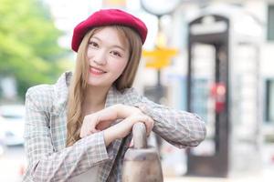 Asian beautiful woman who wears suit and red cap with bronze hair sits on chair in the city outdoors on a sunny morning. photo