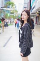 Portrait of a beautiful, long-haired Asian female in a black pattern coat with braces on teeth walking and smiling outdoors in the city. photo