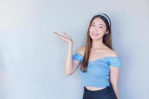 hermosa joven mujer asiática de cabello castaño largo con una camisa azul está actuando como muestra de mano presentando algo en el fondo. foto