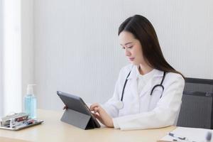 Serious professional doctor wearing white coat and stethoscope holding modern touchscreen gadget using digital tablet computer at work. photo