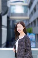 Portrait of a beautiful, long-haired Asian woman in a black pattern coat with braces on teeth standing and smiling outdoors in the city. photo
