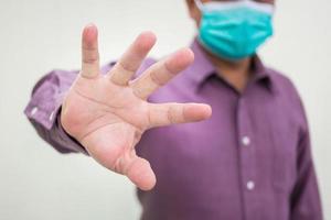 Male hand making stop covid sign gesture while he wears a medical face mask photo