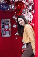 hermosa mujer asiática de pelo largo con una túnica amarilla y una sonrisa feliz parada frente a una cabina telefónica roja con el tema de celebrar la navidad y feliz año nuevo. foto