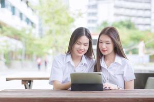 Two young Asian woman students are consulting together and using a tablet to search information for a study report. photo