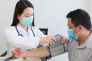 Professional Asian woman doctor uses a blood pressure meter with a man patient photo