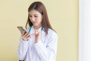 Asian woman doctor examine report document of patient to plan the next treatment. She look at the smartphone in her hand while working at hospital. photo