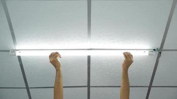 close-up van de hand van een man die een lange led-lamp op het plafond installeert.
