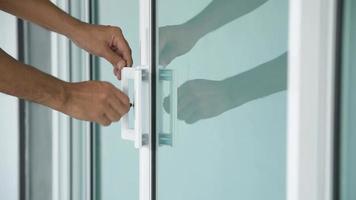 close-up da mão do homem abrindo uma porta de vidro com uma chave.