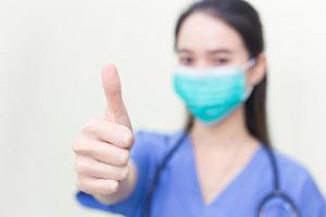 Asian woman wears medical coat and medical face mask who shows thump up as good sign on white background. photo