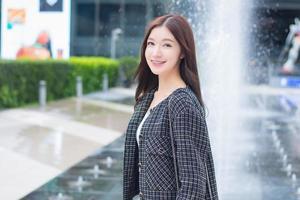 Portrait of a beautiful, long-haired Asian woman side face in a black pattern coat with braces on teeth standing and smiling outdoors in the city. photo