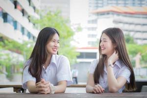 dos jóvenes estudiantes asiáticas están consultando juntas para buscar e intercambiar información para un informe de estudio en la universidad con el edificio de la facultad como fondo. foto