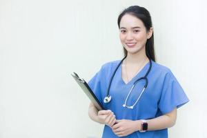 una hermosa doctora asiática de pie sonriendo con una camisa azul de laboratorio, sosteniendo documentos de pacientes en la mano. concepto de salud foto