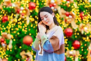 hermosa mujer asiática en un suéter colorido se encuentra feliz. en su mano sostenía una luz frente al árbol de navidad. con bokeh como fondo en el tema de las celebraciones de navidad y año nuevo foto