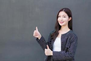 Asian professional working woman who wears black suit with braces on teeth is pointing hand to present as thump up on the dark gray wall. photo