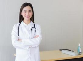 joven y hermosa doctora asiática parada con los brazos cruzados feliz y sonriendo en el hospital. vistiendo una túnica blanca y un estetoscopio foto