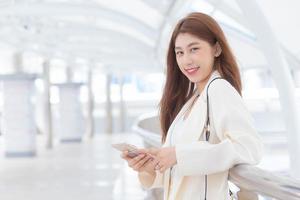 Portrait with blur background of long hair beautiful young Asian professional woman in white suit with smiling face posing looking at camera while working outdoors the office. photo