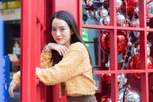 Asian beautiful woman long haired  wearing a yellow robe smile happy standing in beside of a red telephone booth In the theme of celebrating Christmas and Happy New Year. photo