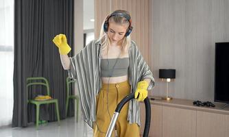 niña divirtiéndose mientras limpia el piso con una aspiradora. mujer feliz haciendo tareas domésticas en casa disfruta de la música con auriculares. foto