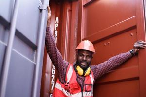 feliz ingeniero afroamericano sonriendo cuando está parado en el almacén de contenedores, el trabajador obtiene seguridad social y seguro, día laboral y concepto de negocio de éxito. foto