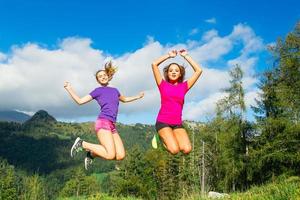 Two young pretty girls jumping on the grass in a mountain scener photo