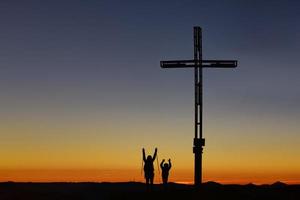 Mom with child on top of the mountain near the cross raise their arms in victory photo