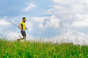 Young man runs down in the green grass while practicing Nordic walking photo