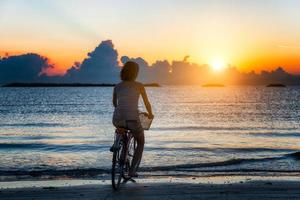 niña en bicicleta en el mar durante el amanecer foto