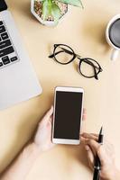 Hand holding empty screen Smart phone on business desk office with copy space, Top view photo
