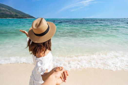 joven pareja viajera tomándose de la mano relajándose y disfrutando en la hermosa playa tropical de arena blanca con espuma de olas y mar transparente, vacaciones de verano y concepto de viaje foto