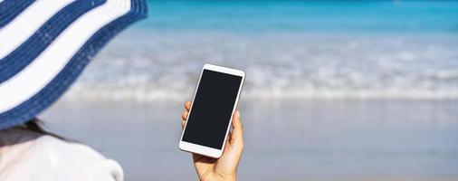 Young asian woman traveler using her smartphone at tropical sand beach, Summer vacation concept photo