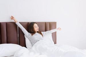 Young asian woman sitting on the bed and stretch oneself in the morning photo