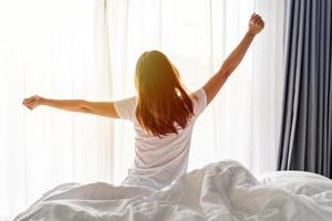 Young asian woman sitting on the bed and stretch oneself in the morning at home photo