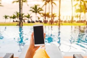 Young woman traveler relaxing and using a mobile phone by a hotel pool while traveling for summer vacation photo