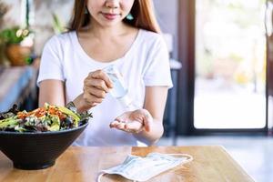 Young woman using alcohol gel sanitizer to avoid infections corona virus and bacteria before meals in restaurant, New normal lifestyle concept photo