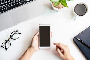 Hand holding empty screen Smart phone on business desk office with copy space, Top view photo