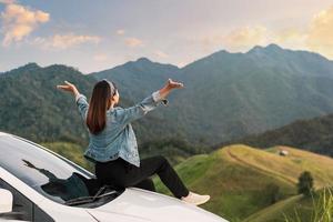 Young woman traveler sitting on a car watching a beautiful mountain view while travel driving road trip on vacation photo