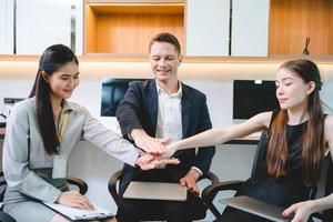 Team of young male and female employees stacking hands on top of each others to depict unity and harmony amongst colleagues for project and positive work environment photo