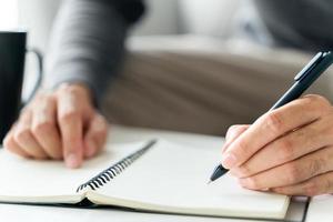 left handed man writes in a notebook on the table photo