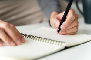 left handed man writes in a notebook on the table photo