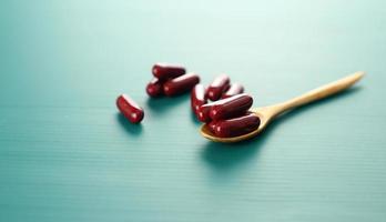 Red vitamin pills on spoon against green photo