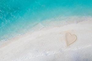 Perfect drawing of heart shape in soft sand beautiful seascape background. Romantic Valentine's day or love beach scene, top aerial view. Romance, honeymoon in vacation, summer travel. Idyllic nature photo