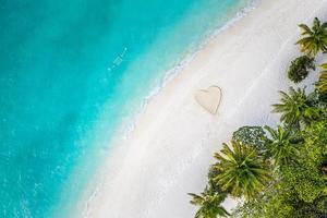Perfect drawing of heart shape in soft sand beautiful seascape background. Romantic Valentine's day or love beach scene, top aerial view. Romance, honeymoon in vacation, summer travel. Idyllic nature photo