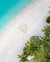 Perfect drawing of heart shape in soft sand beautiful seascape background. Romantic Valentine's day or love beach scene, top aerial view. Romance, honeymoon in vacation, summer travel. Idyllic nature photo