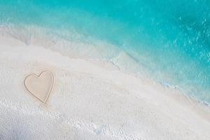 Perfect drawing of heart shape in soft sand beautiful seascape background. Romantic Valentine's day or love beach scene, top aerial view. Romance, honeymoon in vacation, summer travel. Idyllic nature photo