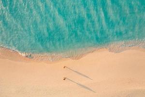 Aerial view of amazing beach with couple walking in sunset light close to turquoise sea. Top view of summer beach landscape, romantic inspirational couple vacation, romantic holiday. Freedom travel photo