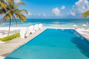 Luxury travel. Beach chair around swimming pool in tropical hotel resort with sea beach background. Exotic holiday and vacation concept photo